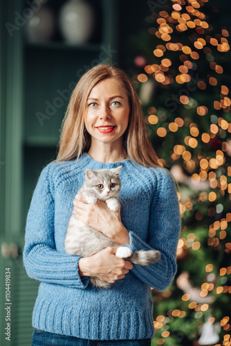 A beautiful woman at home near the Christmas tree with her beloved pet cat
