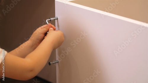 Close-up of a child using an allen key to tighten a screw on white furniture, showcasing diy, home improvement, and fostering child development photo