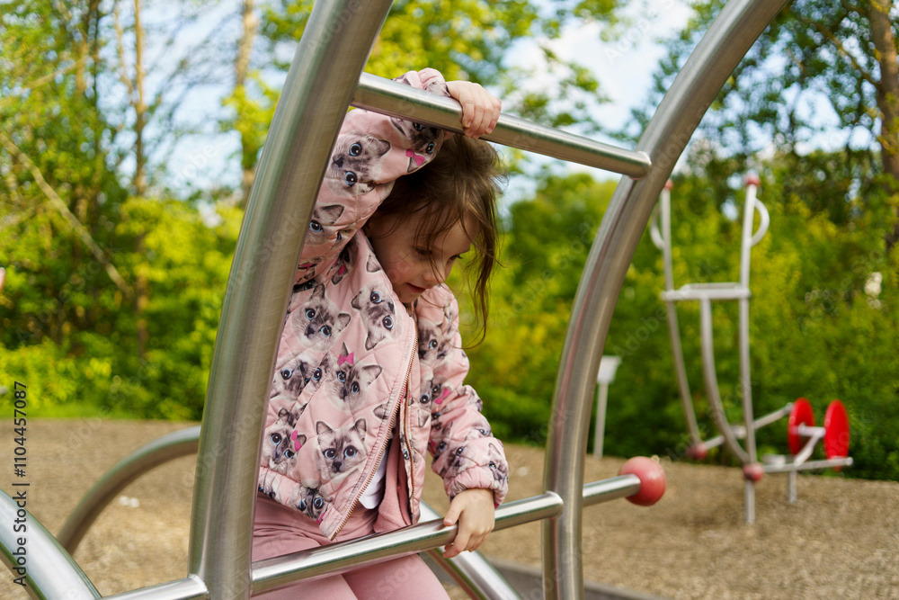 Obraz premium Little girl with long hair climbing on playground in summer. Healthy active mischievous child concept