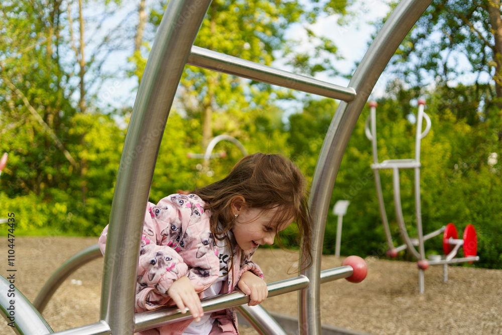 Obraz premium Little girl with long hair climbing on playground in summer. Healthy active mischievous child concept