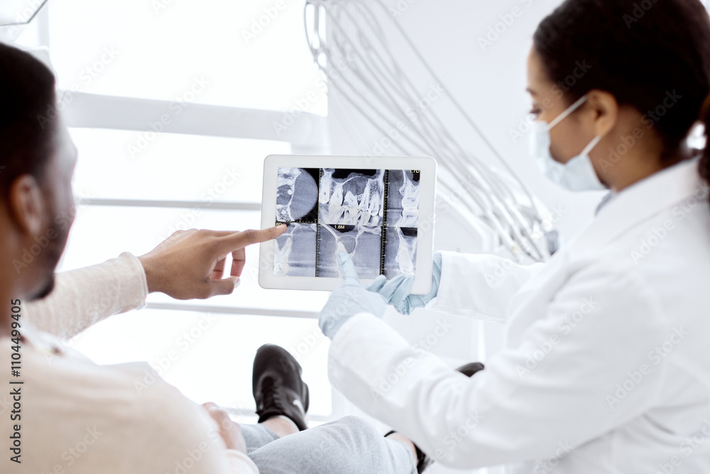 © Prostock-studio - Black female dentist showing xray of teeth treatment process on digital tablet to patient during check up in modern stomatologic clinic, male customer looking at tab computer screen, closeup