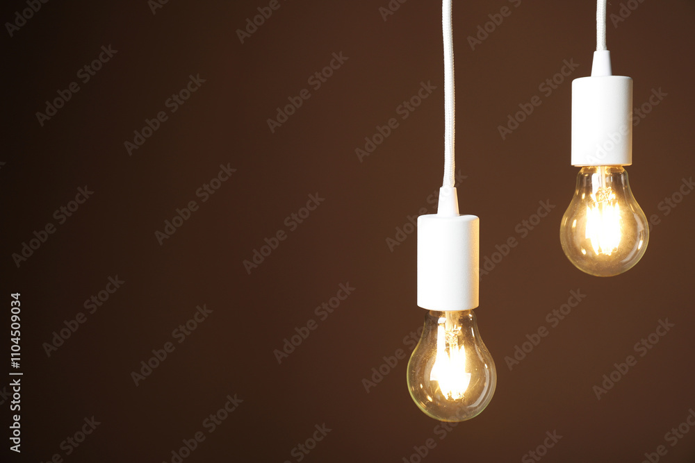 Light bulbs hanging on cords against brown background, space for text Light bulbs hanging on cords against brown background, space for text