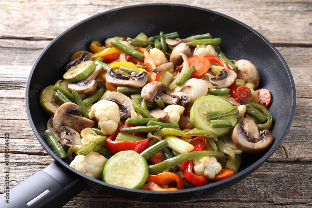 Different vegetables and mushrooms in frying pan on wooden table, closeup Different vegetables and mushrooms in frying pan on wooden table, closeup