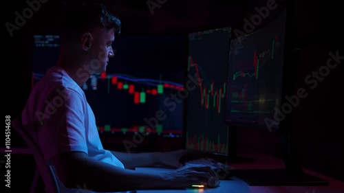 Pensive investor male working from home office as financial analyst, monitoring stock market data on computer screens in dark room, illuminated by colorful glow of charts and graphs, slow motion. photo