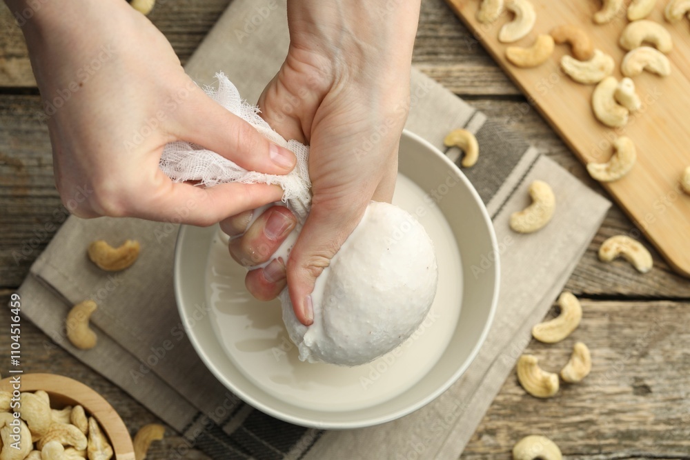 Woman straining cashew milk into bowl at wooden table with nuts, top view Woman straining cashew milk into bowl at wooden table with nuts, top view