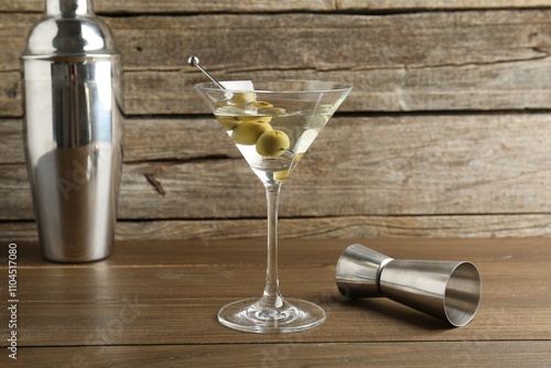 Martini cocktail with olives in glass, shaker and jigger on wooden table photo