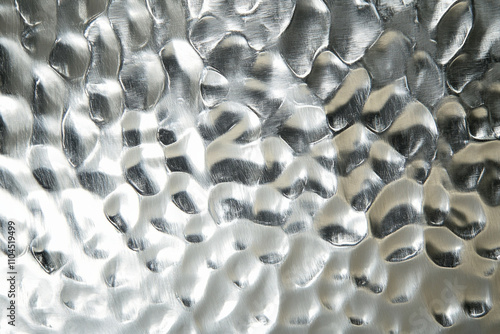 A hammered silver surface with irregular dimples and a reflective sheen, creating a unique handcrafted texture. photo