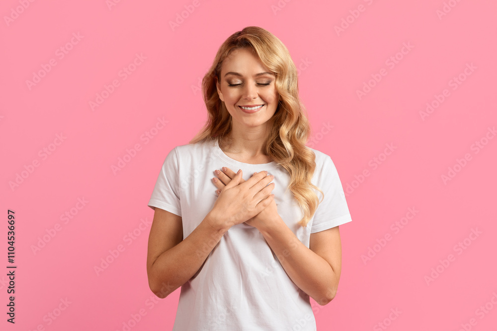A young woman stands with a serene smile, placing her hands over her heart. She radiates warmth and gratitude in front of a vibrant pink background, creating a joyful atmosphere. A young woman stands with a serene smile, placing her hands over her heart. She radiates warmth and gratitude in front of a vibrant pink background, creating a joyful atmosphere.