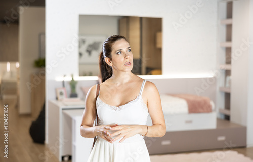 Watchful middle-aged woman buyer staring attentively at pieces of furniture during shopping