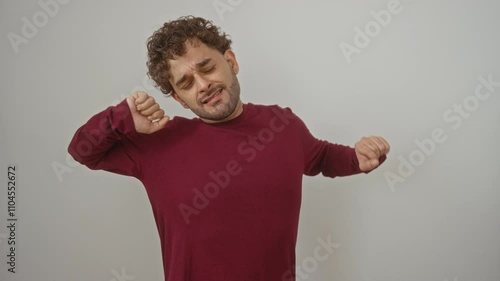 Young hispanic man standing and yawning, tired expression in sleepy isolation over white background, wearing t-shirt with hand covering mouth in natural portrait showing sleepiness and boredom