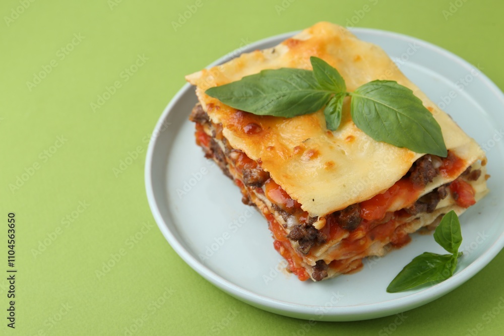 Delicious cooked lasagna with basil on light green table, closeup. Space for text Delicious cooked lasagna with basil on light green table, closeup. Space for text