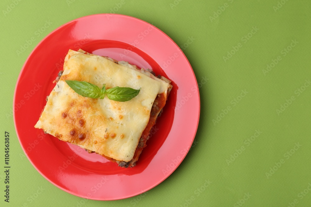 Piece of delicious cooked lasagna with basil on green background, top view. Space for text Piece of delicious cooked lasagna with basil on green background, top view. Space for text
