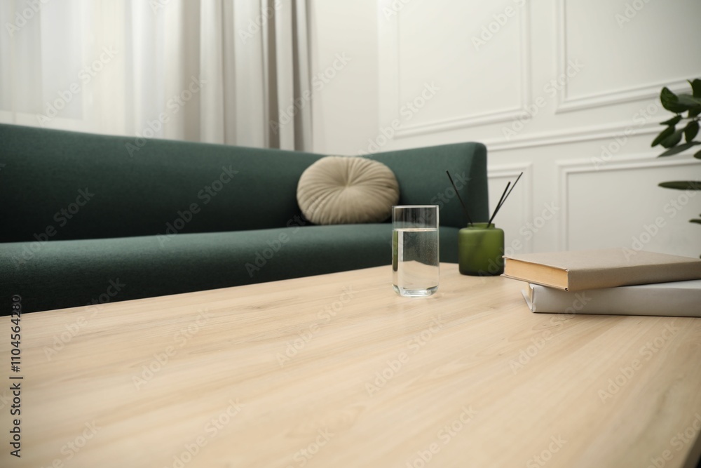 Books, glass of water and reed diffuser on wooden coffee table near sofa in living room, closeup Books, glass of water and reed diffuser on wooden coffee table near sofa in living room, closeup