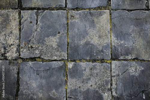 Worn stone pavement texture, aged gray slabs with visible cracks and faint mossy patches photo