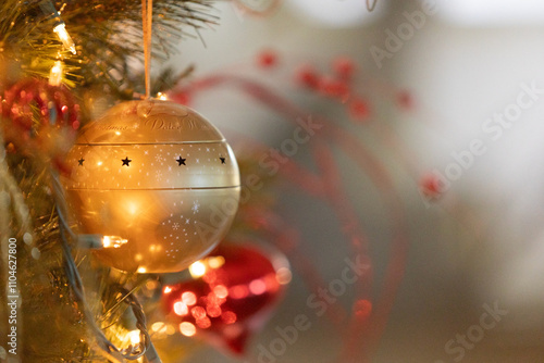 Close up of gold bauble ornament hanging on Christmas tree next to gold lights and red ornaments photo