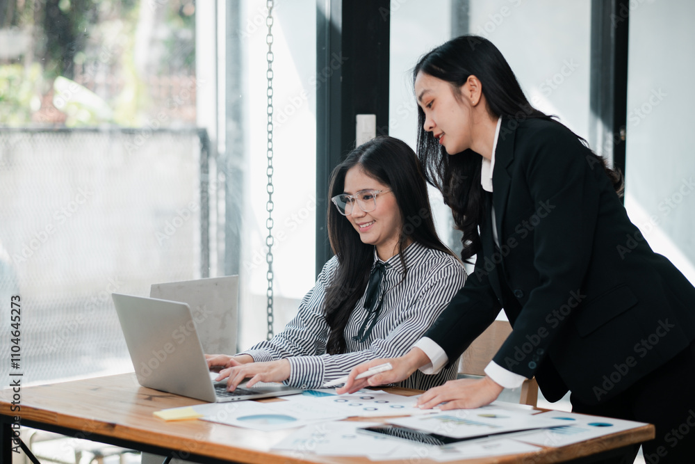 Two businesswomen working together in a contemporary office, discussing ideas with a laptop and paperwork. Two businesswomen working together in a contemporary office, discussing ideas with a laptop and paperwork.