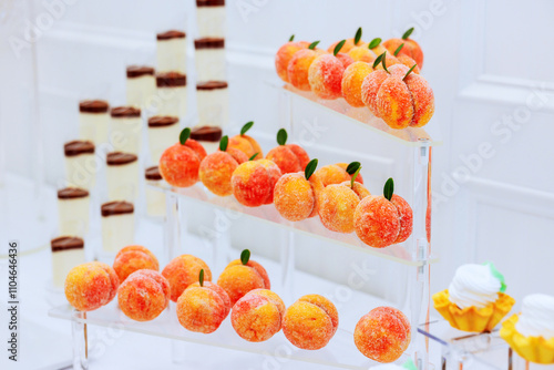 Delicious dessert peach shaped sweets are beautifully arranged on clear multi tiered stand, at festive celebration event photo