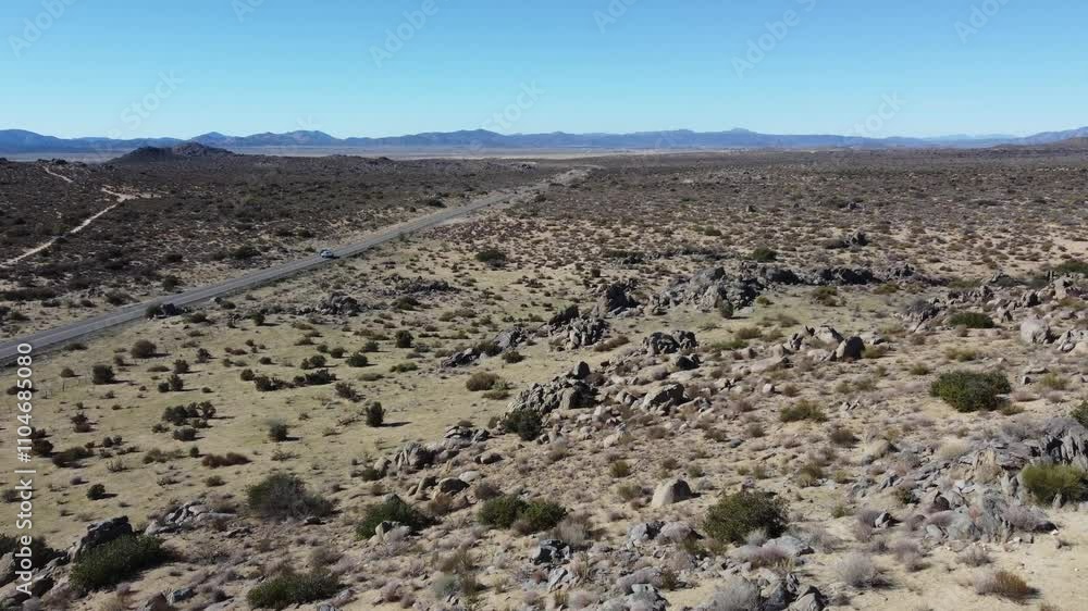 Aerial swoops from desert rock ridge to follow cars on remote highway Aerial swoops from desert rock ridge to follow cars on remote highway