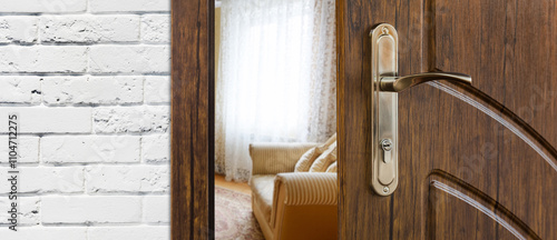 Half opened door handle closeup, entrance to a living room. View of sofa. Welcome, privacy concept. Door lock with keys, white brick wall, modern interior design. photo