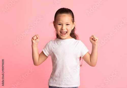 Win Concept. Portrait of excited asian child with raised hands shaking fists over pink background