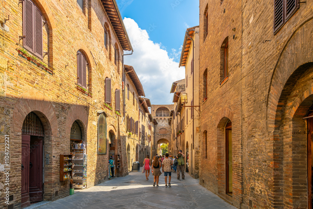 Obraz premium Tourists walk the narrow pedestrian streets near the Porta San Giovanni main gate in the Tuscan hilltop village of San Gimignano, Italy.