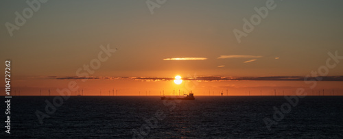 Transport ship and offshore wind farm at sunset on the North Sea horizon. Few clouds, golden sky. Netherlands, Scheveningen, The Hague. photo