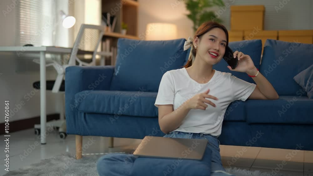 Young woman is sitting on the floor, leaning against a sofa, talking on her phone and gesturing with her hand Young woman is sitting on the floor, leaning against a sofa, talking on her phone and gesturing with her hand
