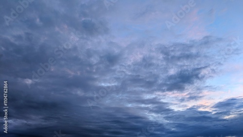 A dramatic sky with a mix of dark, stormy clouds and a vibrant orange sunrise. The clouds create a sense of depth and movement, while the warm hues of the sunset provide a striking contrast.