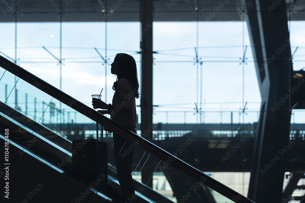 Silhouette standing woman to transit with travel luggage on escalator at international airport terminal Silhouette standing woman to transit with travel luggage on escalator at international airport terminal