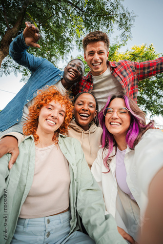 Group of happy teenagers smiling and having fun outdoors, enjoying friendship and diversity while taking a selfie together in a park on a bright sunny day. Young friends smiling and laughing