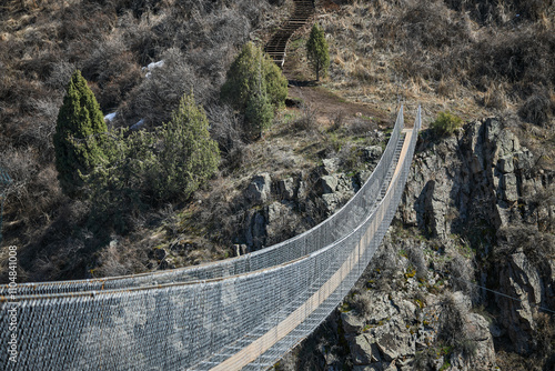 Sky Bridge in Chunkurchak Gorge, Kyrgyzstan. Suspension excursion bridge over gorge. Sightseeing holiday tour. Crossing between two mountains. Dangerous footbridge. Hiking trek, pathway, side view photo