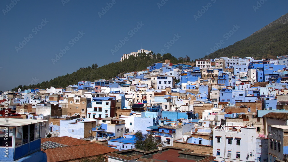 Blue and white buildings in the medina, on a a hill with a forested slope above, in Chefchaouen, Morocco Blue and white buildings in the medina, on a a hill with a forested slope above, in Chefchaouen, Morocco