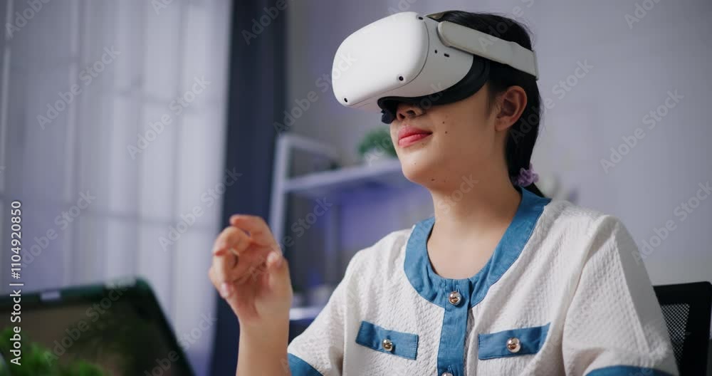 Handheld low angle view shot, Asian freelance woman wearing virtual reality glasses working by touching hands in Metaverse space while sitting at desk in home office. Work from home. Handheld low angle view shot, Asian freelance woman wearing virtual reality glasses working by touching hands in Metaverse space while sitting at desk in home office. Work from home.