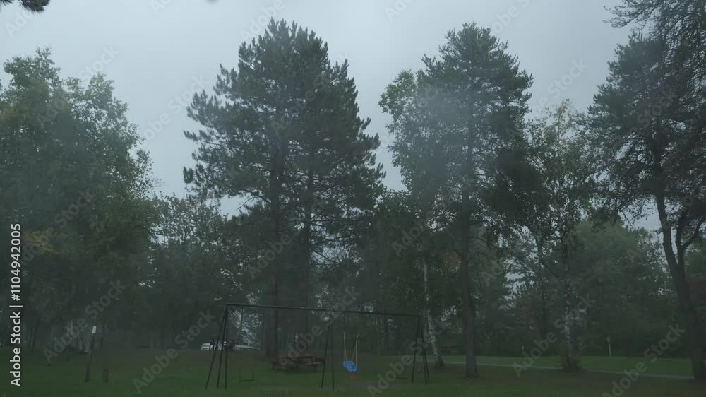 A time-lapse showing rain falling in a peaceful park with a swing set, picnic table, and tall trees swaying under overcast skies, creating a calming atmosphere. A time-lapse showing rain falling in a peaceful park with a swing set, picnic table, and tall trees swaying under overcast skies, creating a calming atmosphere.