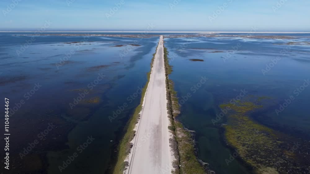 Aerial tilt: Lagoon road leads through shallow blue water to lighthouse Aerial tilt: Lagoon road leads through shallow blue water to lighthouse