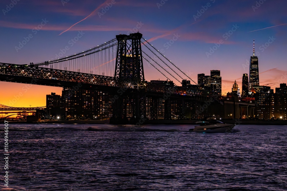Sunset view of the Williamsburg Bridge and New York City skyline with a boat on the East River. Sunset view of the Williamsburg Bridge and New York City skyline with a boat on the East River.