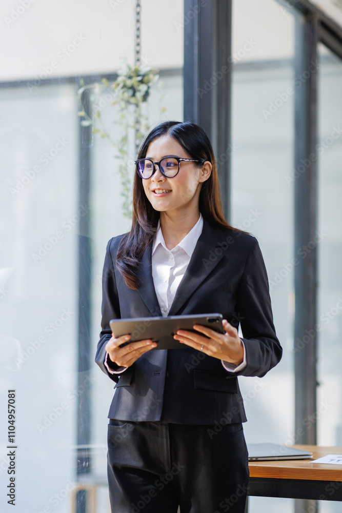 Asian young business woman in the suit executive, happy confidently holding tablet in hand and standing in the office at work. Asian young business woman in the suit executive, happy confidently holding tablet in hand and standing in the office at work.