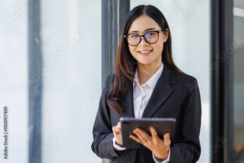 Asian young business woman in the suit executive, happy confidently holding tablet in hand and standing in the office at work.