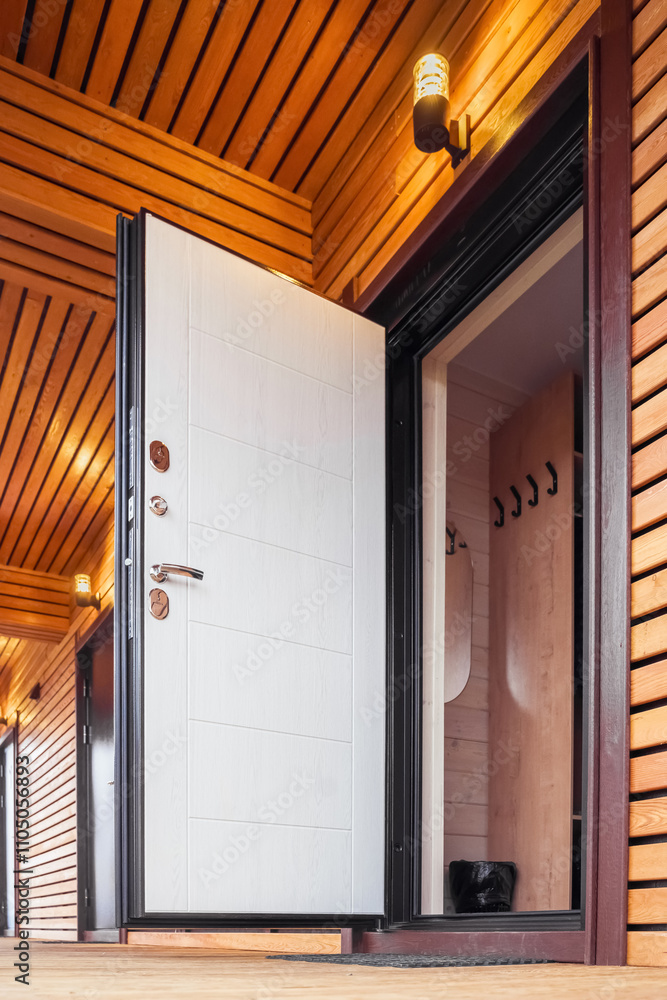 Fototapeta premium Open door. Door stands open, revealing a wooden interior with hooks on the wall. The warm lighting and wooden ceiling create an inviting atmosphere.
