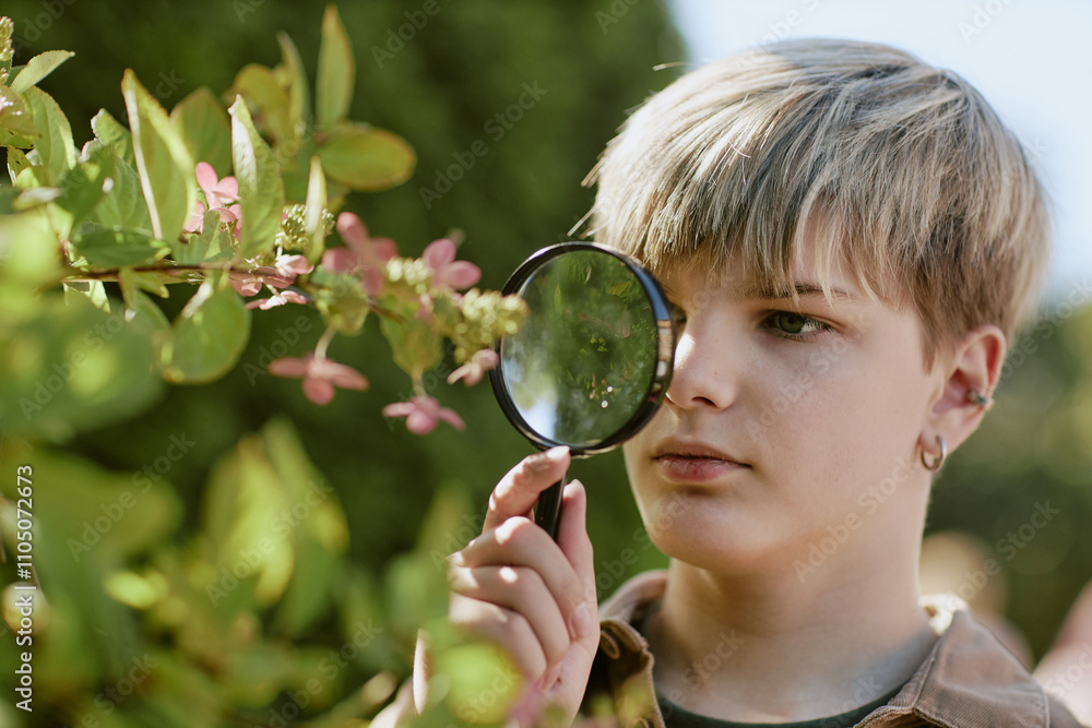 Closeup of Caucasian teen boy holding magnifier looking closer at tree flowers while studying plants in botanical garden Closeup of Caucasian teen boy holding magnifier looking closer at tree flowers while studying plants in botanical garden