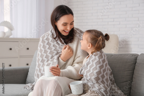 Mother and her little daughter in plaid drinking beverage in living room