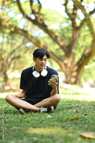 Athletic man taking a break after morning run using smartphone in the city park