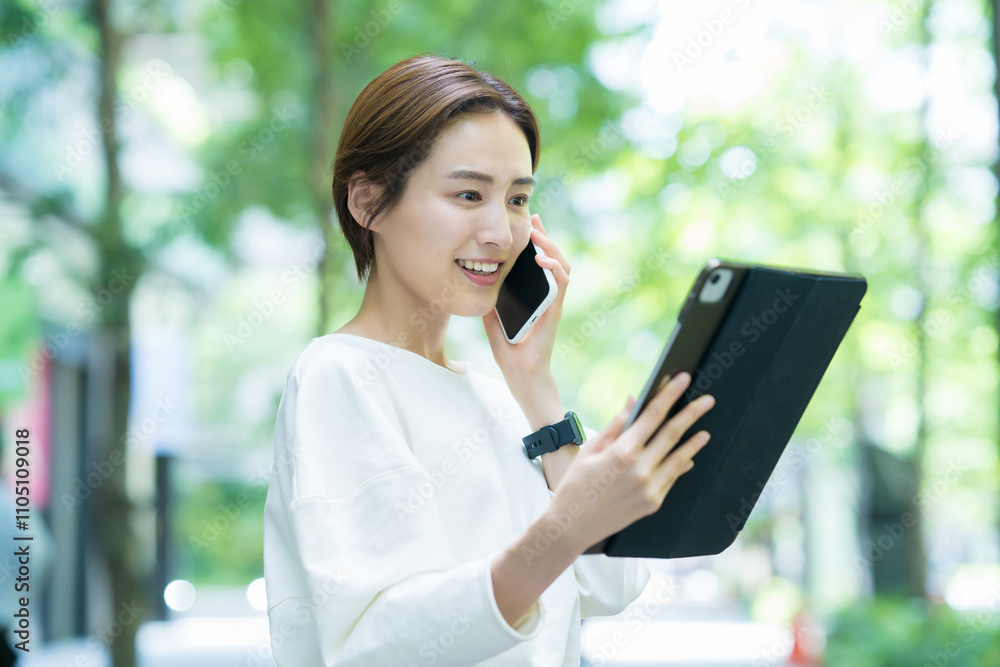 タブレット操作をしながらスマホで通話する女性