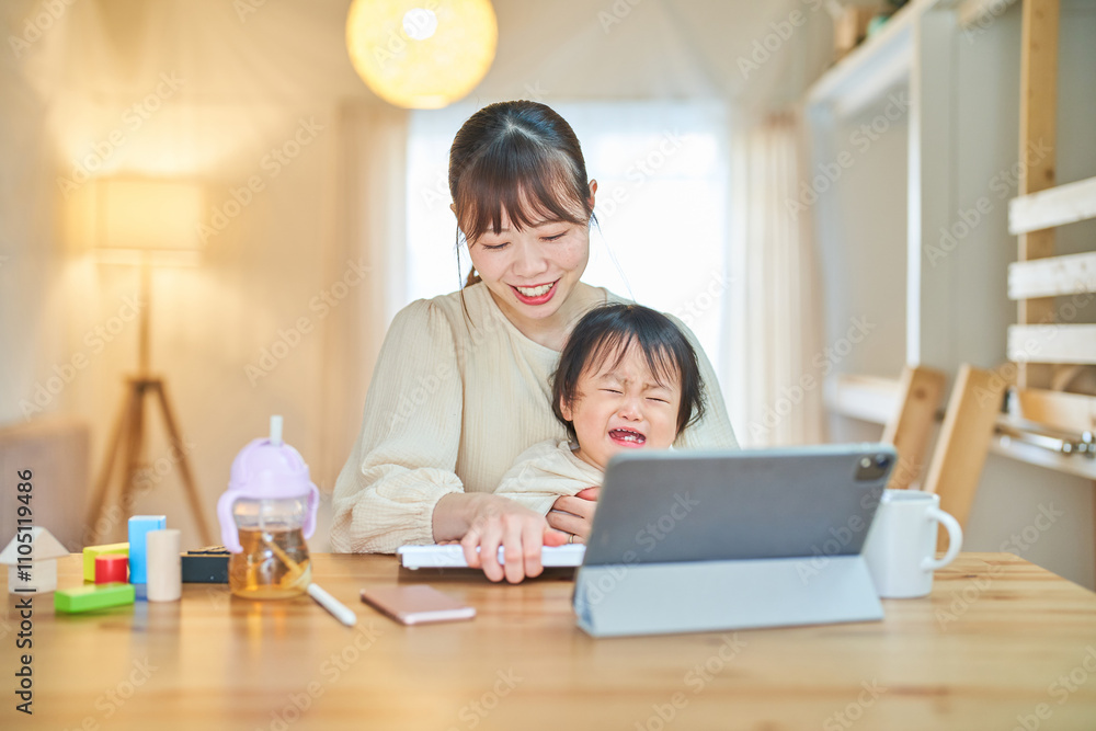 自宅でタブレットPCを操作する女性と泣く幼児 自宅でタブレットPCを操作する女性と泣く幼児