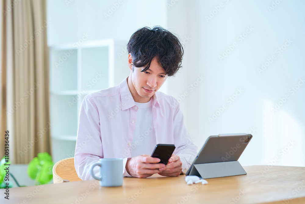 タブレットpcとスマートフォンを見比べる若い男性 タブレットpcとスマートフォンを見比べる若い男性