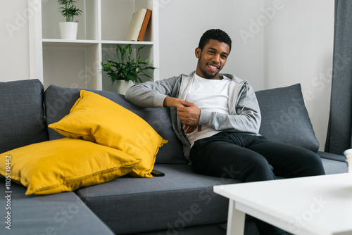 Cheerful curly haired ethnic african american male in casual clothes resting at home on comfortable sofa while watching tv channels or movie during weekend. Tv set, online television and entertiment photo