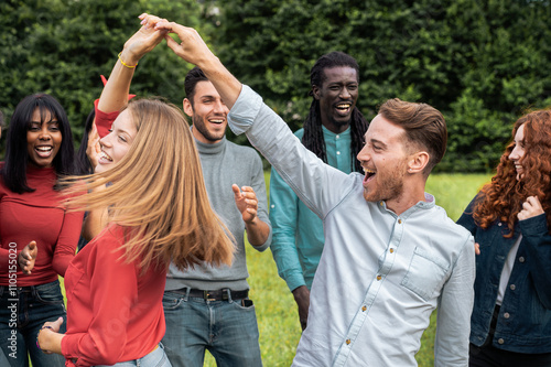 Young diverse friends dancing together, spinning and twirling with authentic joy in summer park