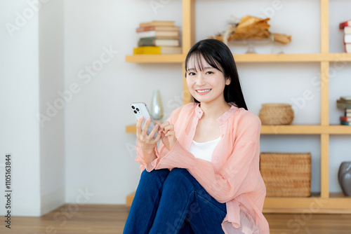 部屋でスマホを操作する若い女性 photo