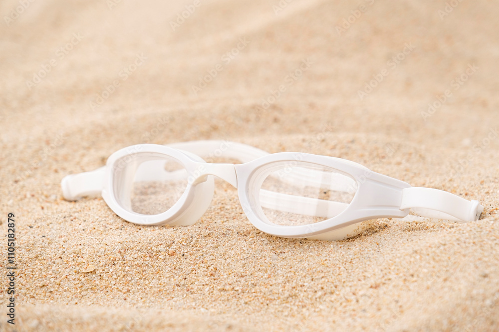 white swimming glasses on sandy beach background white swimming glasses on sandy beach background