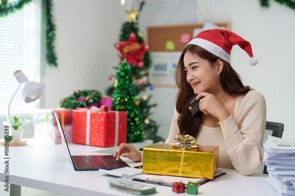 Woman shopping online on Christmas Day sitting at home desk Connecting to laptop and holding credit card in room with Christmas tree decorative gift boxes New Year's celebration ideas. Woman shopping online on Christmas Day sitting at home desk Connecting to laptop and holding credit card in room with Christmas tree decorative gift boxes New Year's celebration ideas.